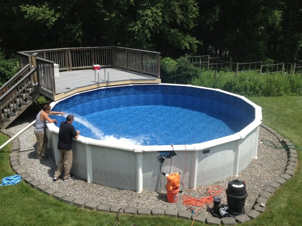 Two installers filling a newly built above-ground swimming pool with an attached wooden deck in a backyard
