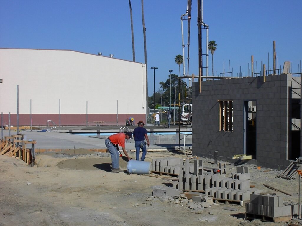Construction crew building a swimming pool and adjacent structure at a job site, illustrating the contractor work behind a pool project