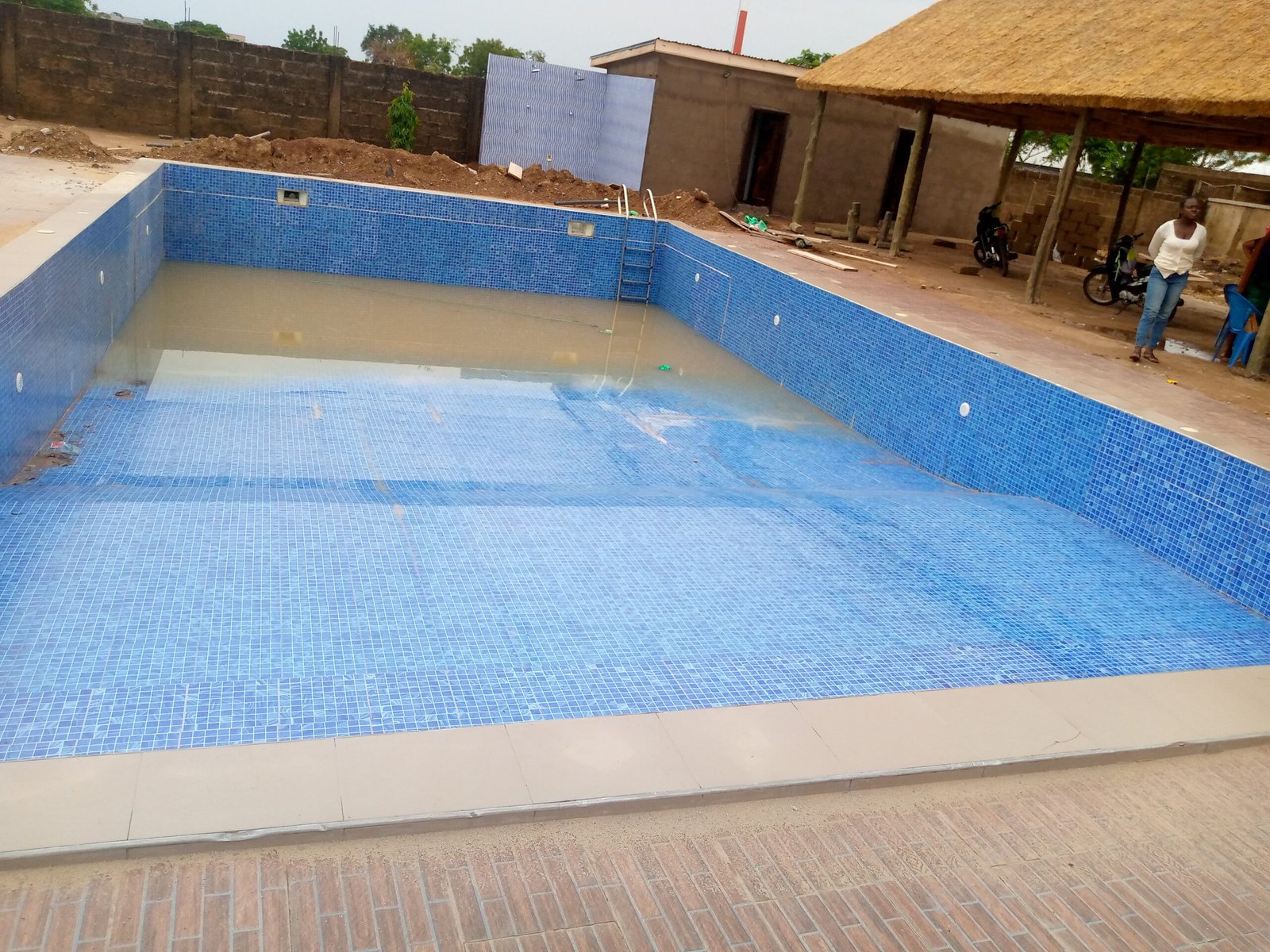 A tiled swimming pool mid-construction with cloudy water and unfinished surroundings, illustrating the gap between how a pool project is imagined and how it actually unfolds
